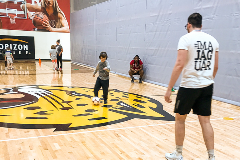 A little boy plays soccer under supervision in the IUPUI gym.