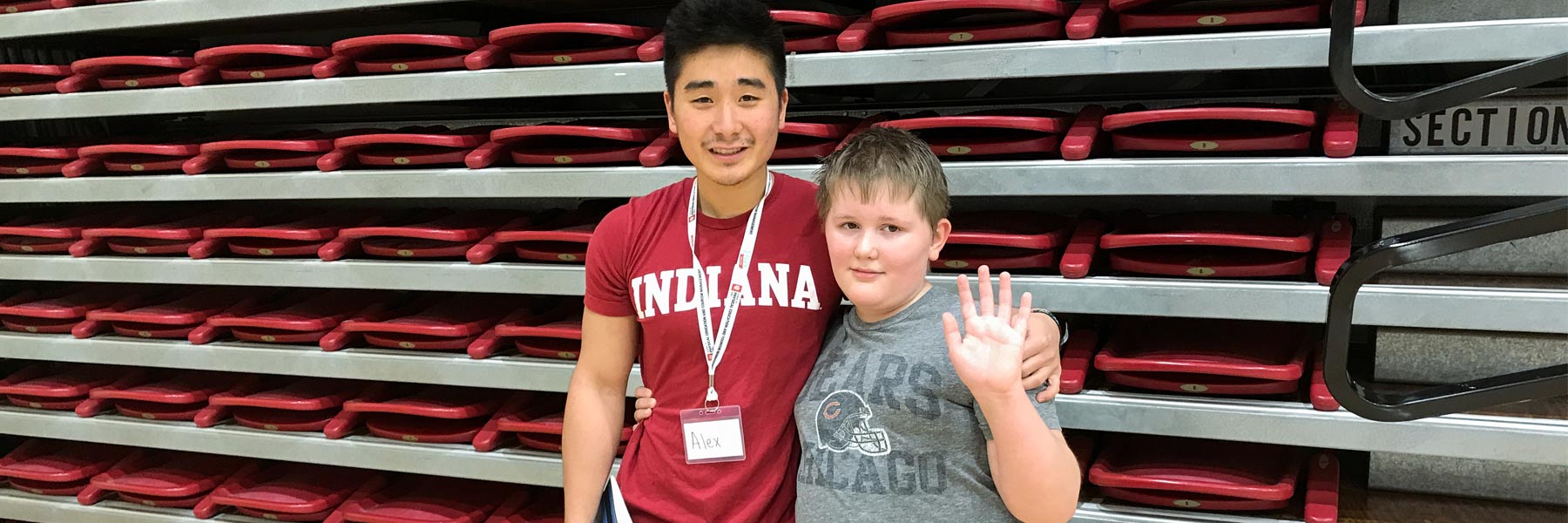 A male AMP instructor in an IU t-shirt poses with his client, an elementary-aged boy waving at camera